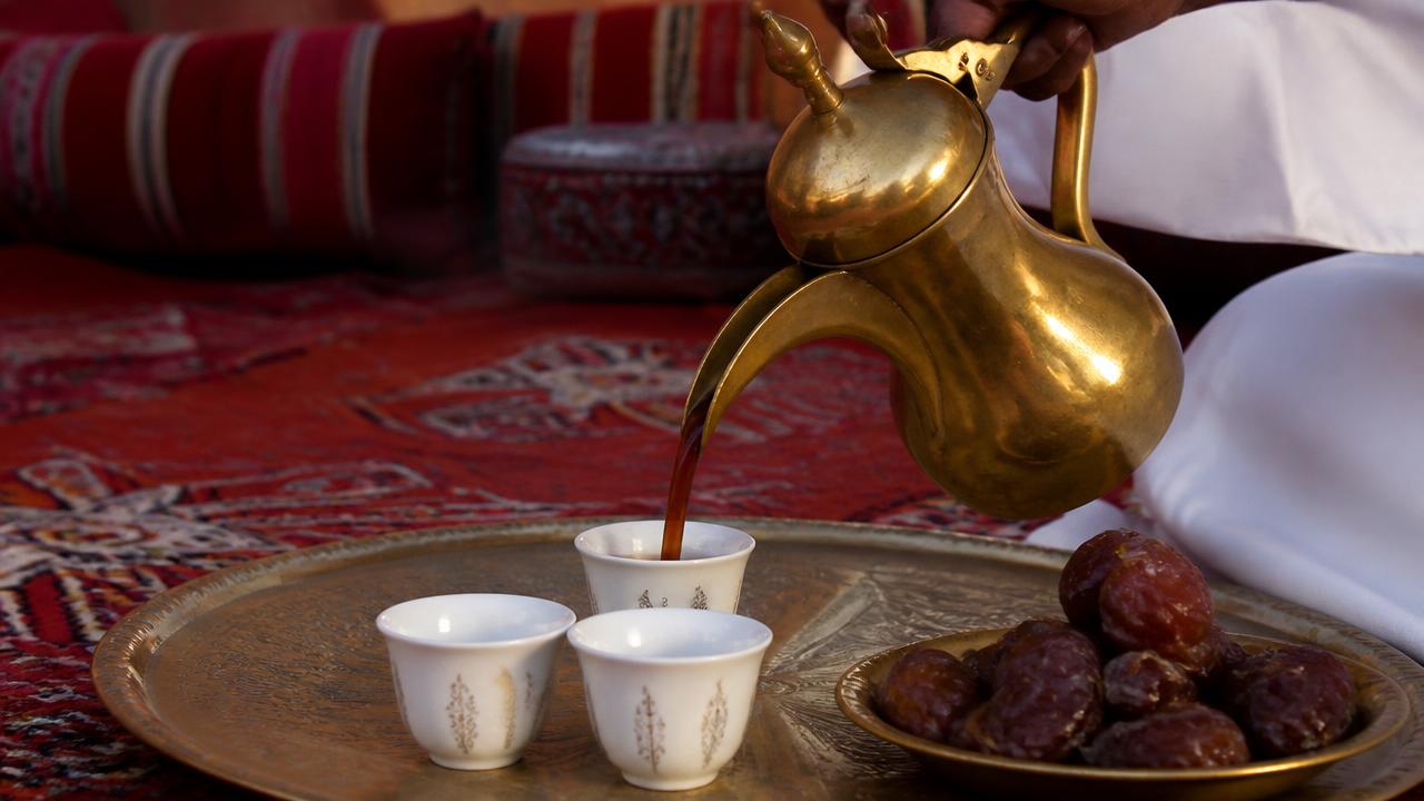 Arabic coffee poured from a brass dallah beside a plate of dates